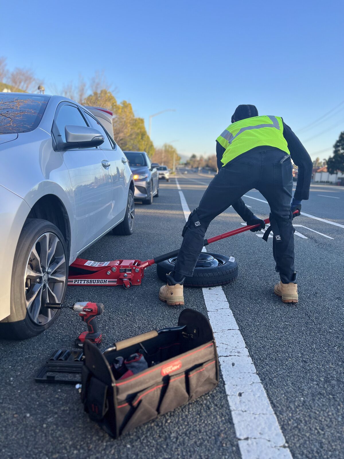 CB Roadside technician in a hi-vis vest changing a tire on a highway shoulder