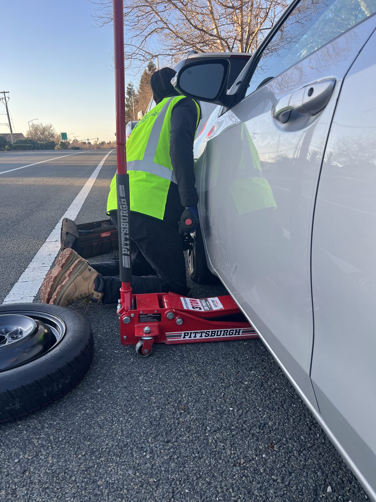 Technician jacking up a car for a tire change on the roadside at dawn